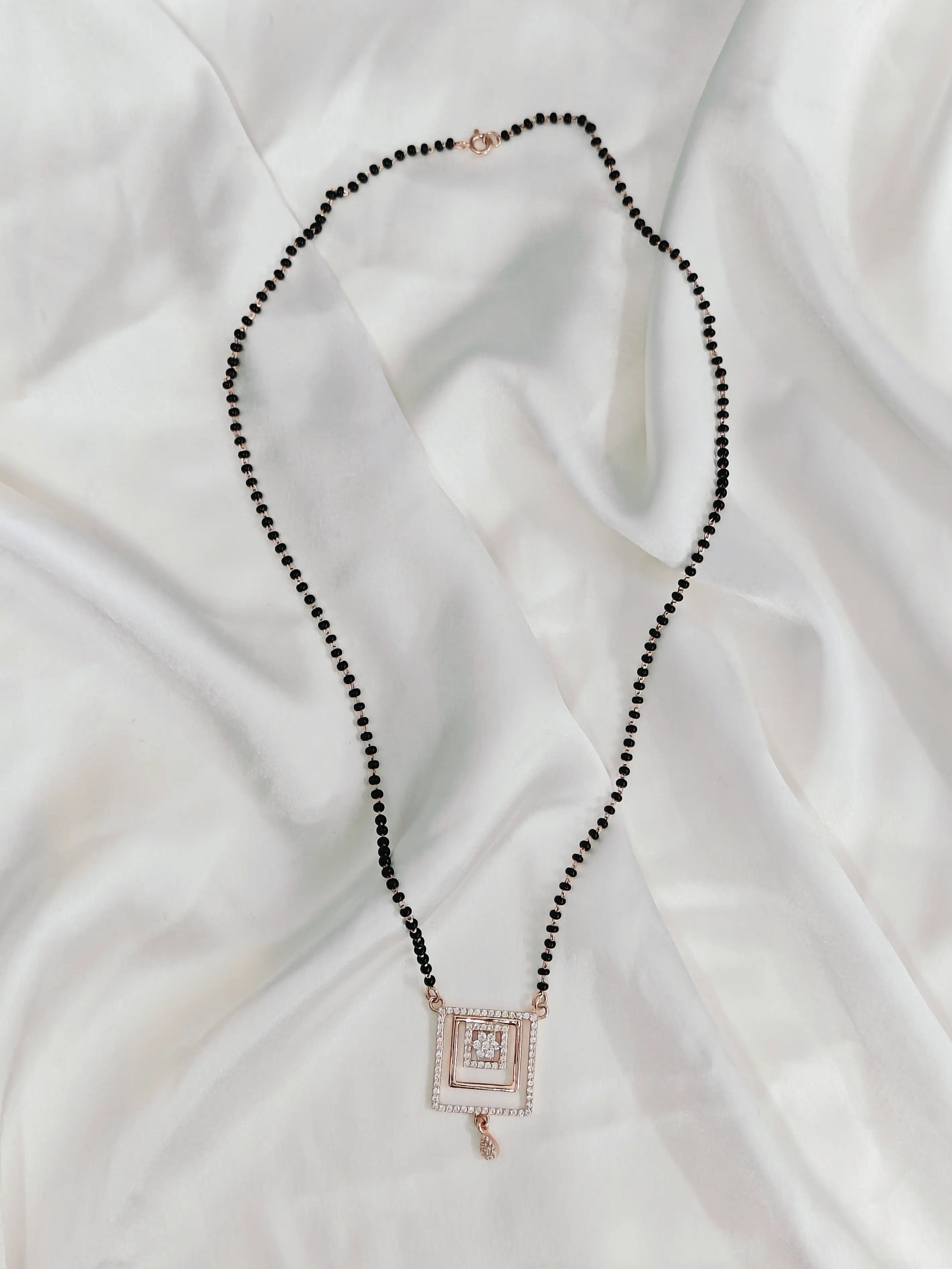 Necklace with black beads and a square pendant on a white fabric background